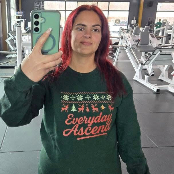 Person wearing a green holiday sweatshirt with 'Everyday Ascent' text in a gym setting

