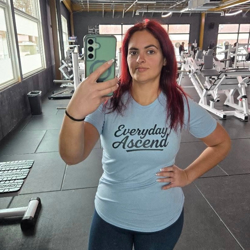 Person taking a mirror selfie in a gym wearing a 'Everyday Ascend' t-shirt.